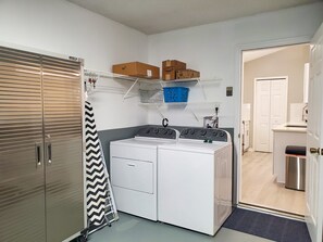 A laundry room with two stacked washers and dryers, a drying rack, and shelves above holding boxes and baskets.