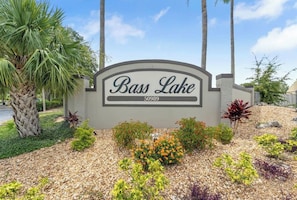 A sign for Bass Lake with a landscaped area featuring various plants and a palm tree.