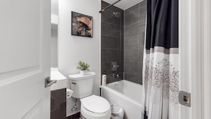 Une salle de bain avec des toilettes, une douche et une baignoire. Un tableau encadré est accroché au mur et une plante en pot est posée sur le comptoir.