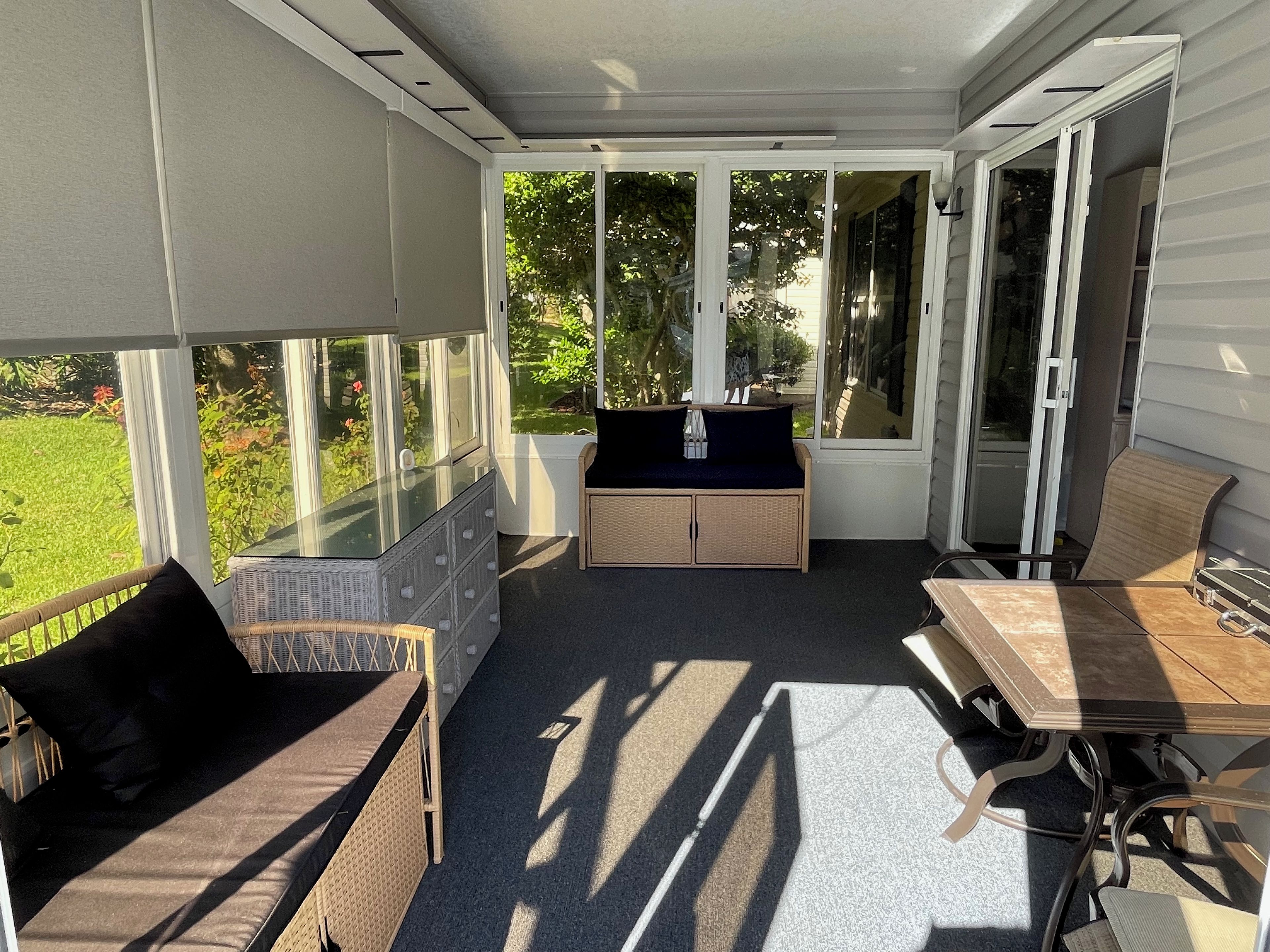 A covered patio with a seating area, a table, and a view of a garden.