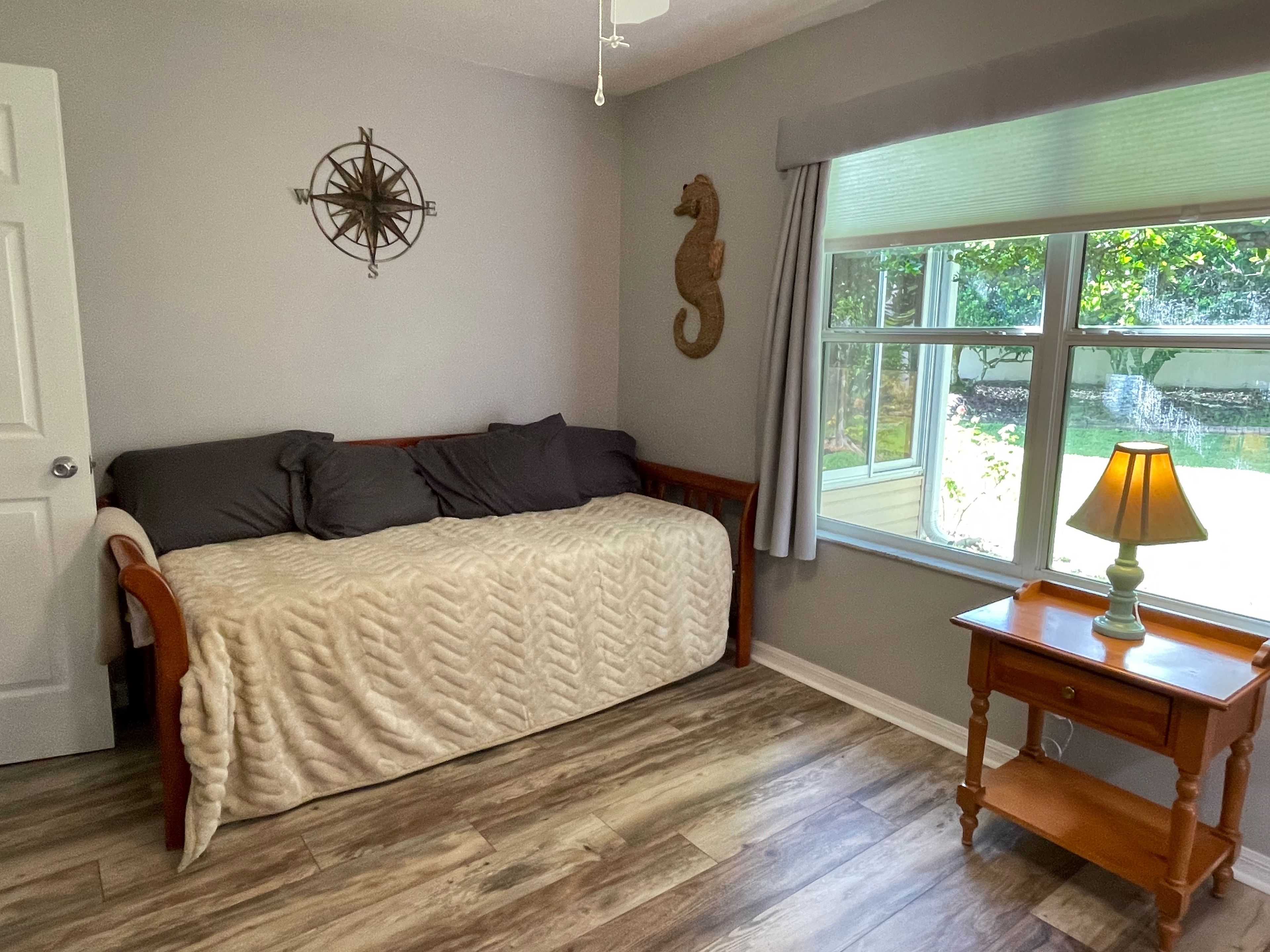 Une pièce avec un lit, un plancher en bois, une fenêtre donnant sur un paysage agréable, une lampe sur une table et un élément décoratif au mur.