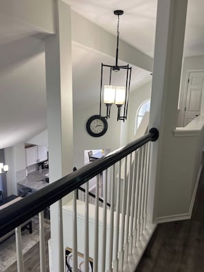 A staircase with white balusters, a chandelier, and a clock on the wall. - Cozy home, Pool access between Sea-word & Sixflags (San Antonio)