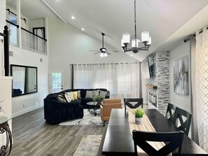A spacious living area with a black sofa, a dining table, and a ceiling fan. - Cozy home, Pool access between Sea-word & Sixflags (San Antonio)