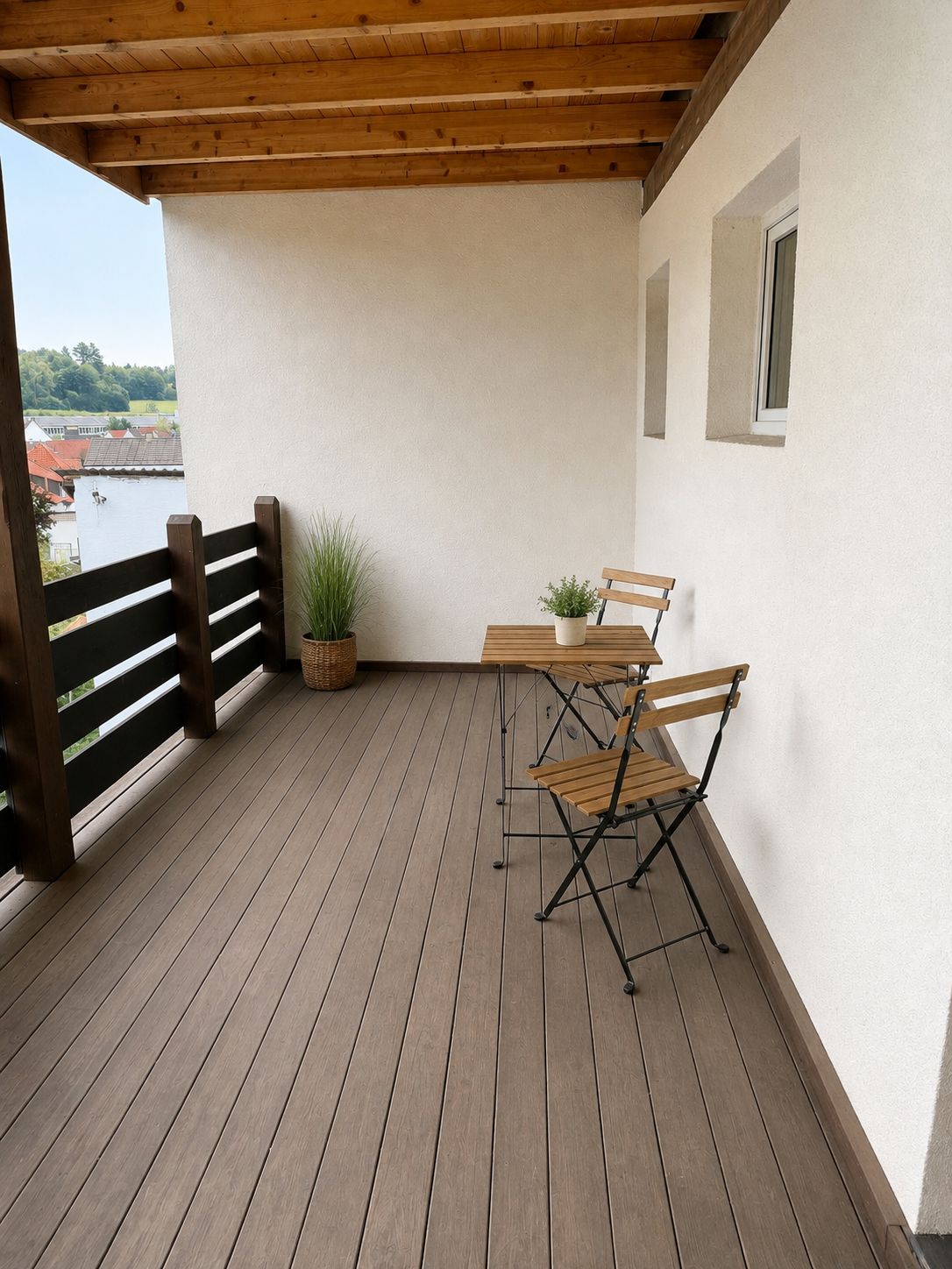 A wooden deck with a table and chairs, a potted plant, and a view of a body of water.