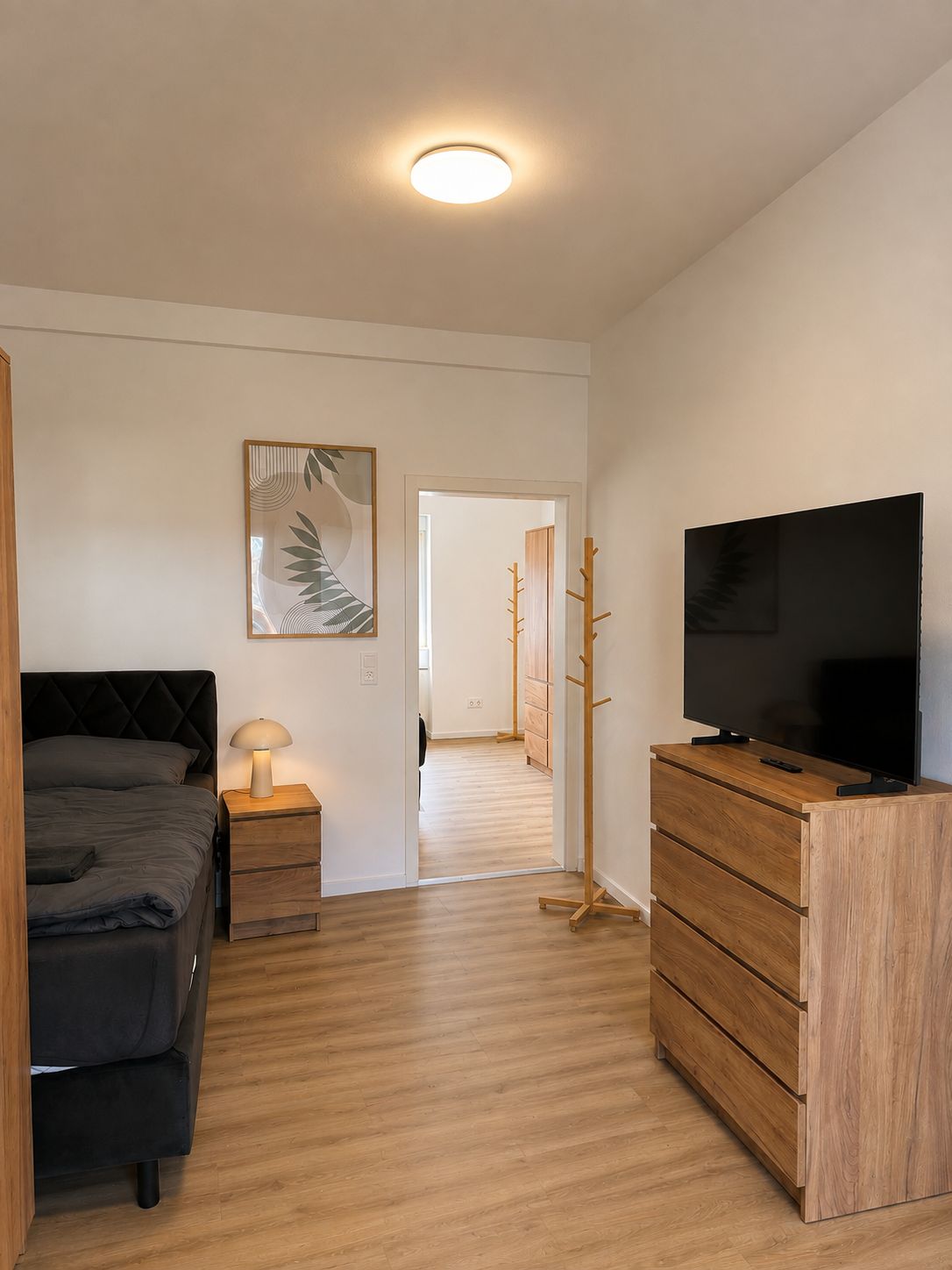 Ein Schlafzimmer mit Bett, Nachttisch, Lampe, Fernseher und Kommode.