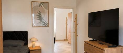 A bedroom with a bed, bedside table, lamp, TV, and a dresser.