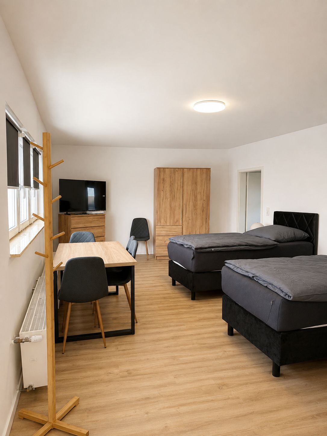 Une pièce de taille modeste, comprenant une table en bois, deux chaises, un téléviseur, une armoire et deux lits.