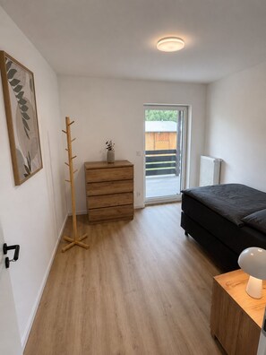 Ein Schlafzimmer mit einem Bett, einem Schminktisch, einem Kleiderständer, einer Heizung und einer Tür zu einem Balkon.