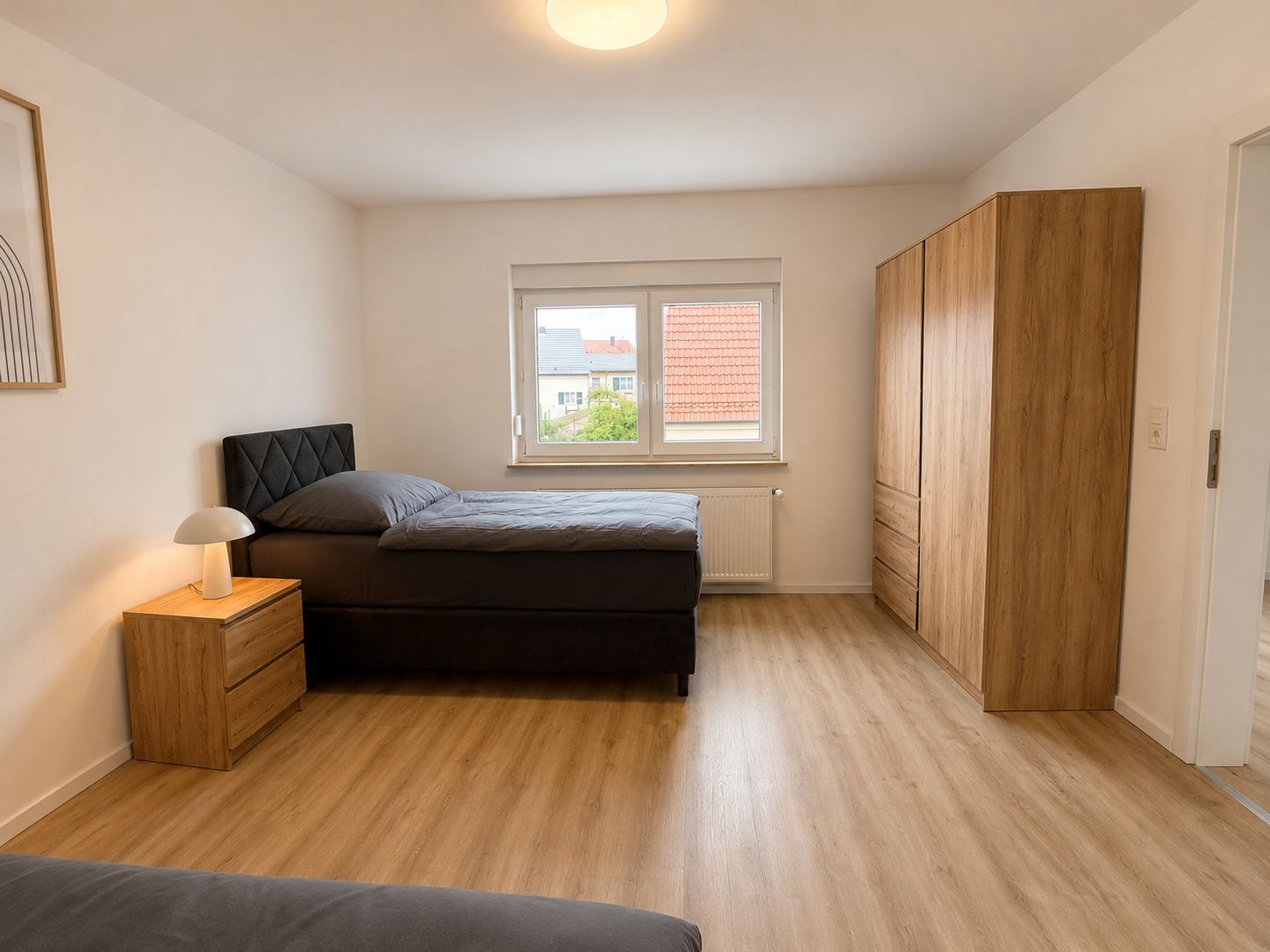 A bedroom with a bed, a nightstand, a window, and a wardrobe.