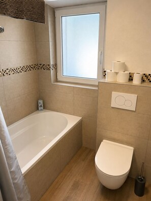 A bathroom with a bathtub, toilet, and a window. - Mühlhausen Ground Floor Apartment for Workers and Vacationers (Mühlhausen)