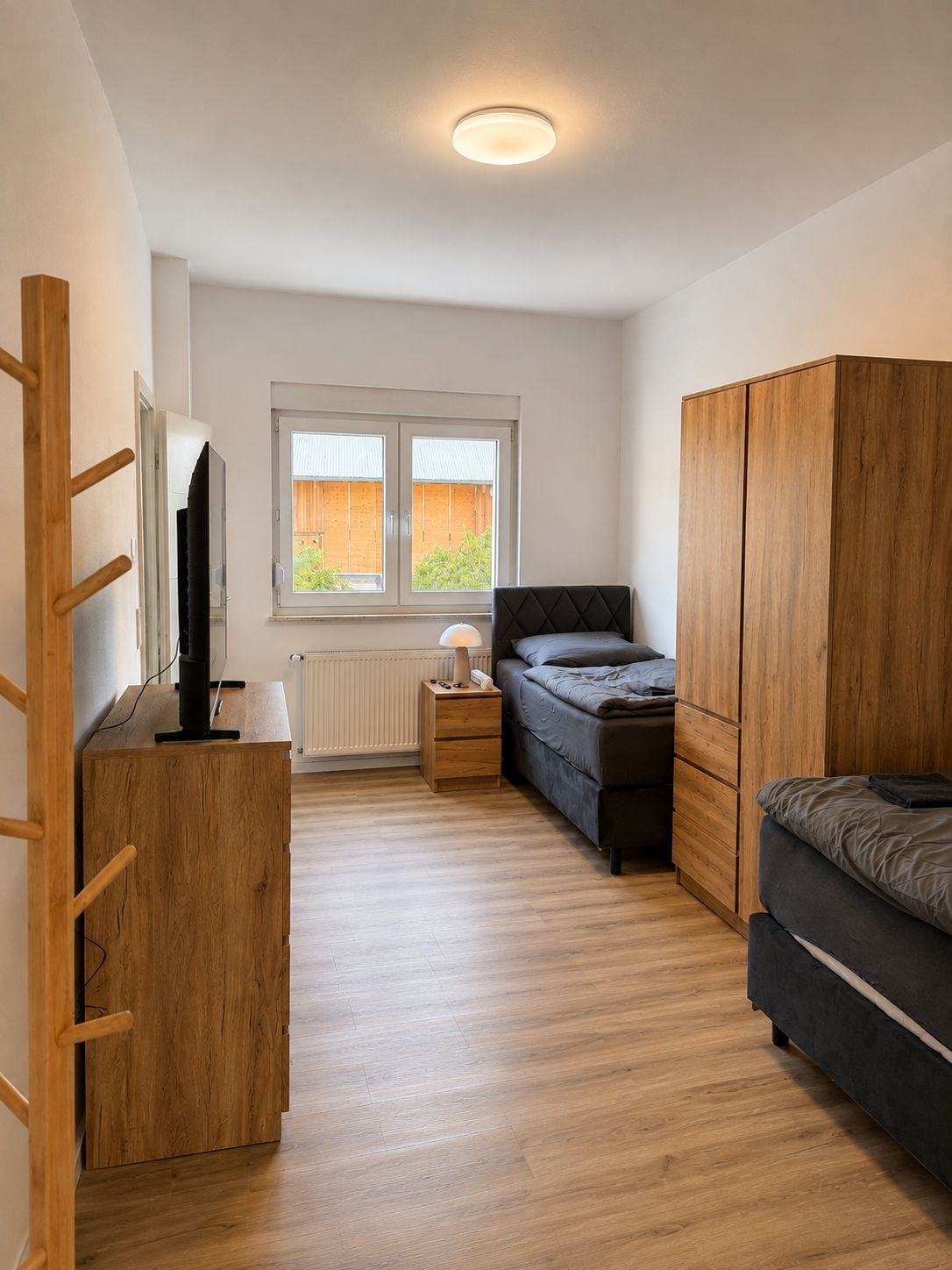 Une chambre à coucher comprenant un lit, une armoire, un bureau avec un ordinateur et une fenêtre donnant sur un mur de briques.