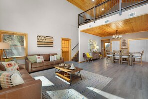 A spacious living room with a high ceiling, a staircase, and a dining area. - The West Nest - Ellijay,GA (Ellijay)