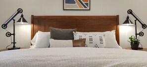 A neatly made bed with a patterned pillow, a brown pillow, and a white pillow. There are two black desk lamps on either side of the bed. - WFH Retreat at Jackson Market (Culver City)