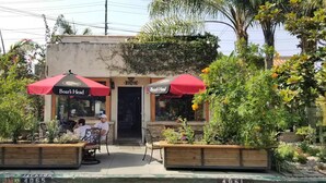 A restaurant with outdoor seating, red umbrellas, and a wooden planter with flowers. - WFH Retreat at Jackson Market (Culver City)