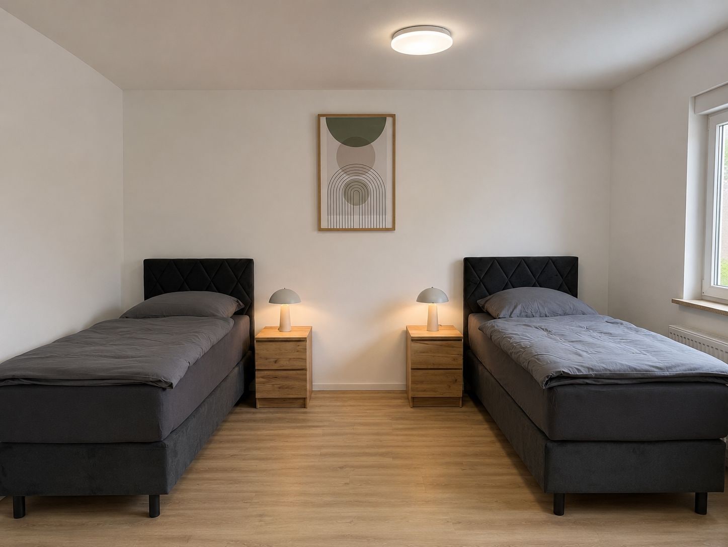 Ein Schlafzimmer mit zwei Betten, Holznachttischen, einer Deckenleuchte und einem gerahmten Kunstwerk an der Wand.