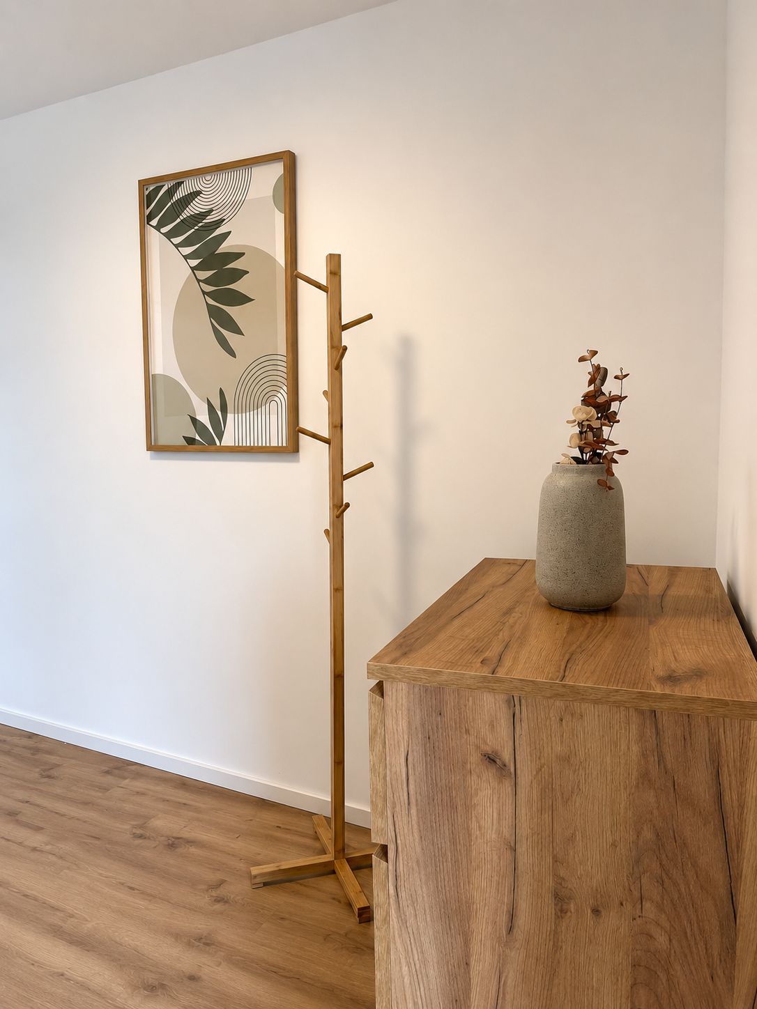 A wooden floor lamp with a leaf-patterned artwork on the wall beside it.