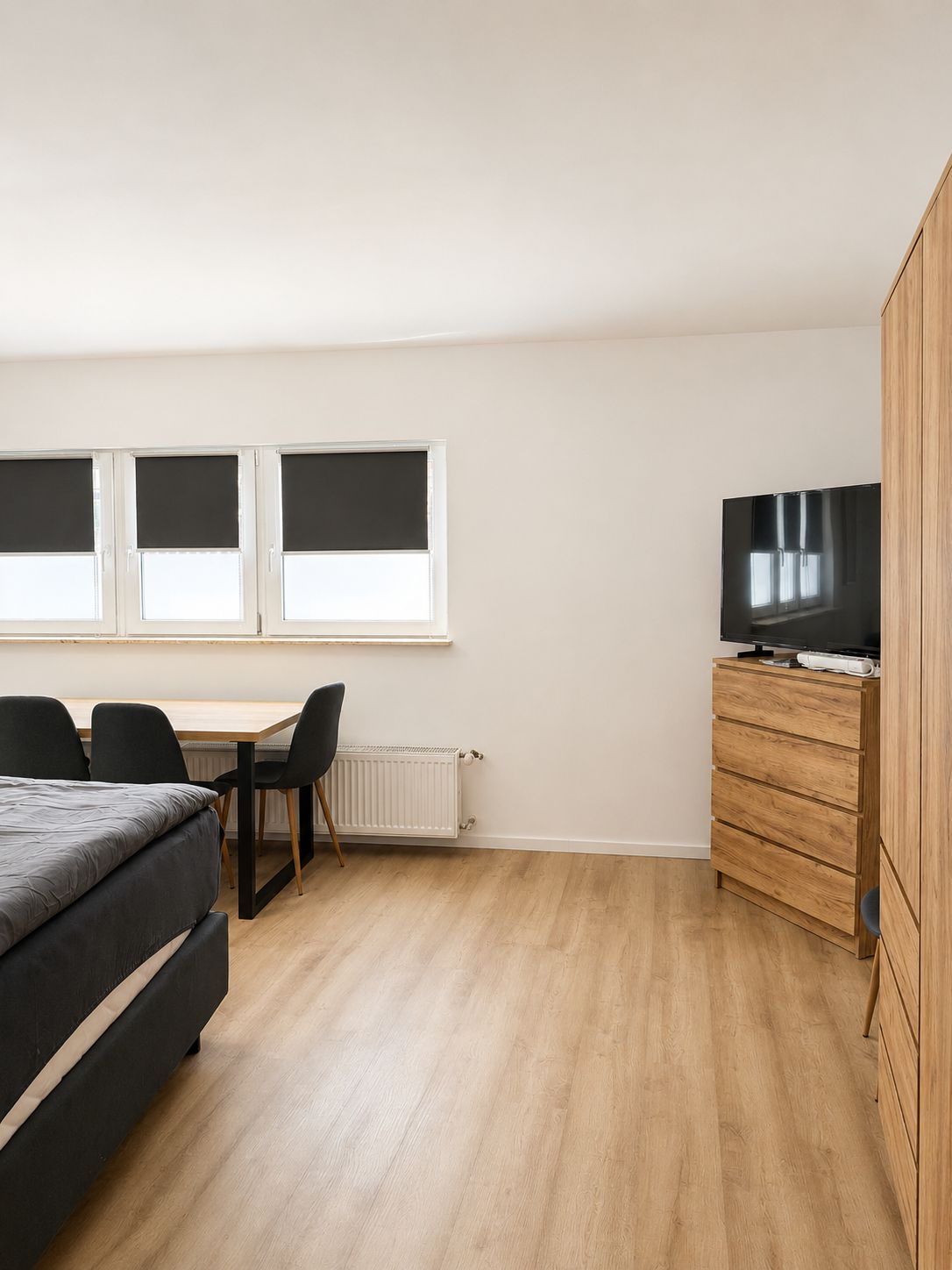 A bedroom with a bed, a desk, a chair, a dresser, and a television.