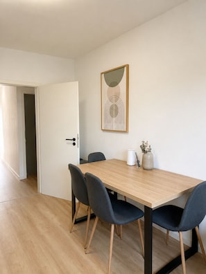 A dining area with a wooden table, four grey chairs, a white door, and a framed abstract artwork on the wall. - Mühlhausen OG Apartment for Workers and Vacationers (Mühlhausen)