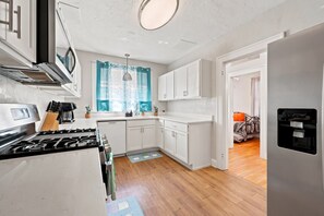 A compact kitchen with white cabinets, a stove, and a water dispenser. - Walk to UF  Shands Ultimate Tailgate House (Gainesville)