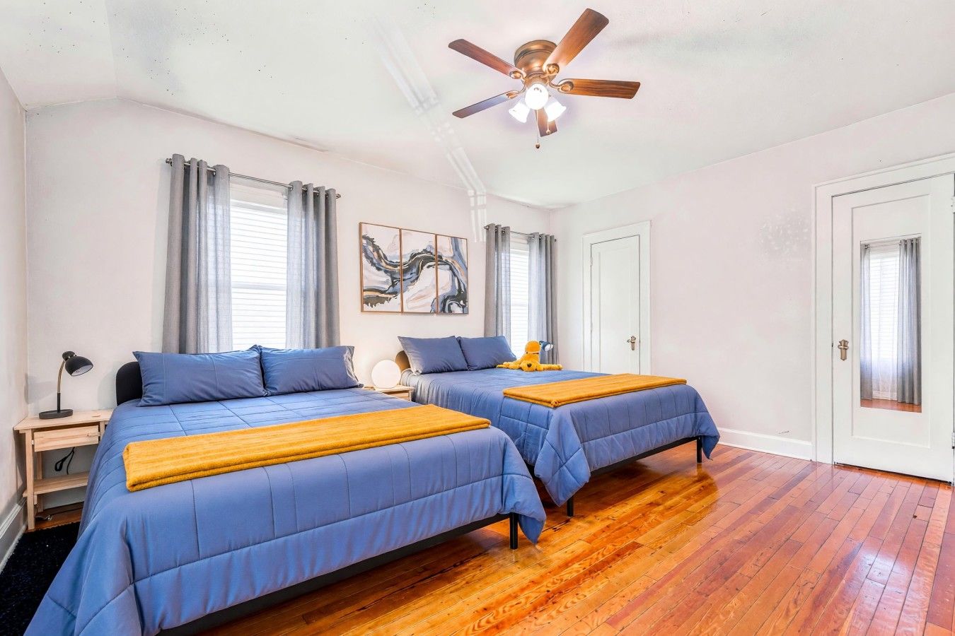 A bedroom with two beds, a ceiling fan, and a wooden floor.