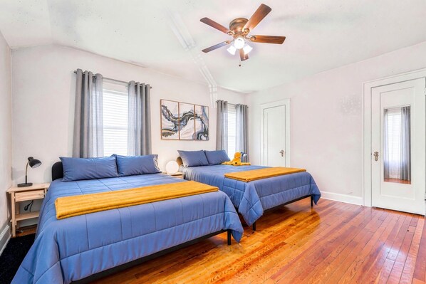 Quarto com duas camas, ventilador de teto e piso de madeira.