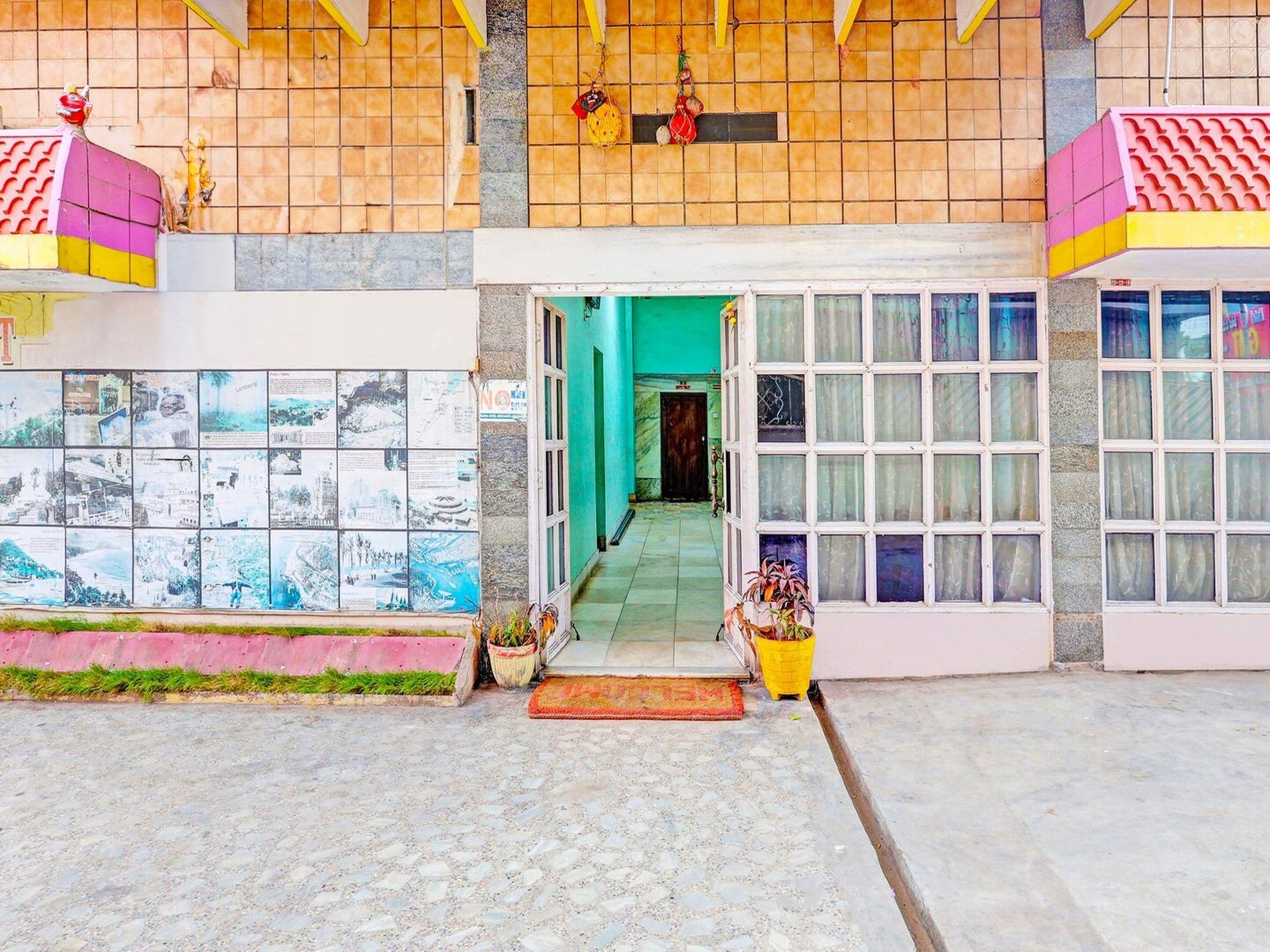 Une entrée d’immeuble avec une façade recouverte de carreaux, une porte verte et un sol carrelé.