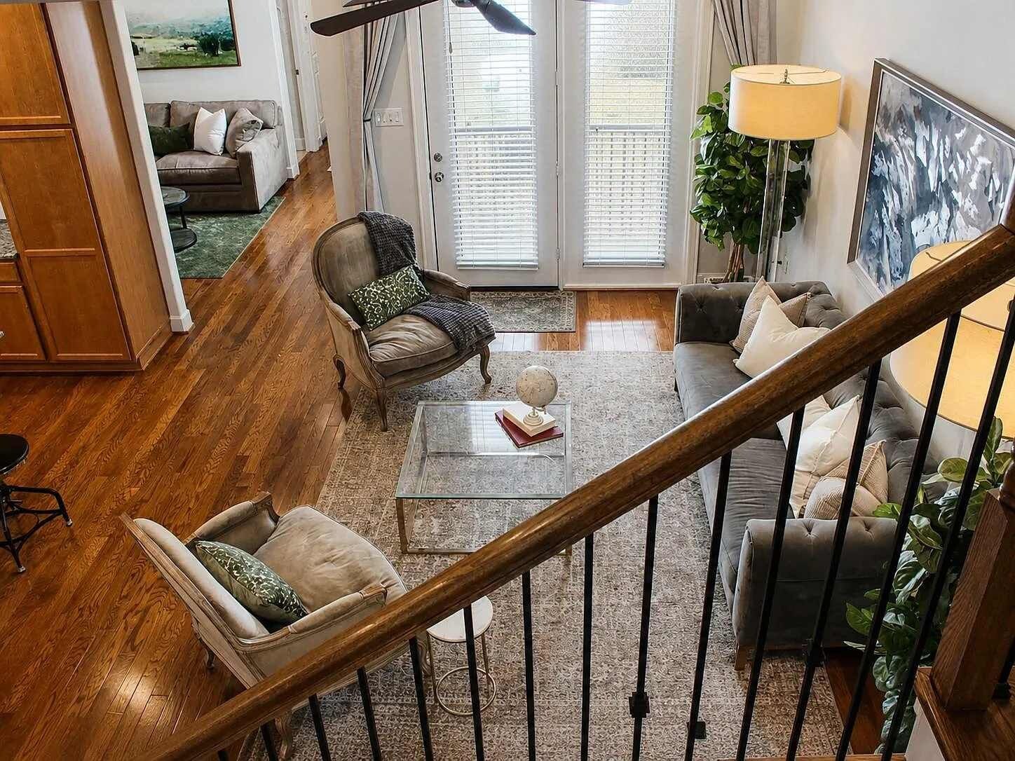 A spacious living room with a wooden floor, a staircase, and a view of the outdoors through large windows.