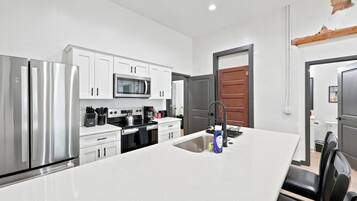 A modern kitchen with stainless steel appliances, white cabinetry, and a central island with a sink.
