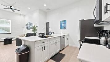A modern kitchen with white cabinetry, a black trash bin, a ceiling fan, and a stainless steel stove.