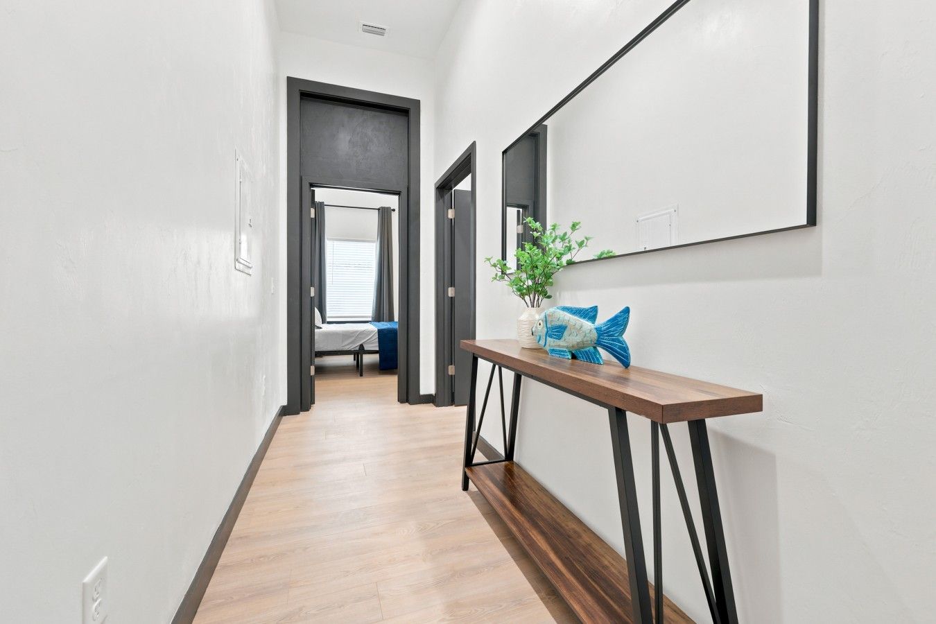 Un couloir avec un plancher en bois, une console ornée d’un poisson décoratif et, au fond, un lit.