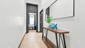 A hallway with a wooden floor, a console table with a decorative fish, and a bed in the background.
