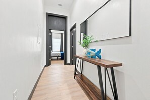 Un pasillo con piso de madera, una consola con un pez decorativo y una cama al fondo.