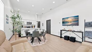 A modern living room with a dining area, a kitchen in the background, and a large painting on the wall.