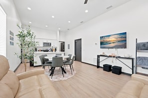 Un salón moderno con comedor, una cocina al fondo y un cuadro grande en la pared.