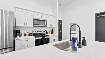 A modern kitchen with white cabinetry, a stainless steel refrigerator, a microwave, an oven, and a sink with a faucet.