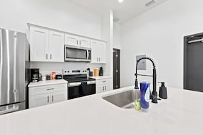 Una cocina moderna con armarios blancos, un refrigerador de acero inoxidable, un microondas, un horno y un lavabo con grifo.