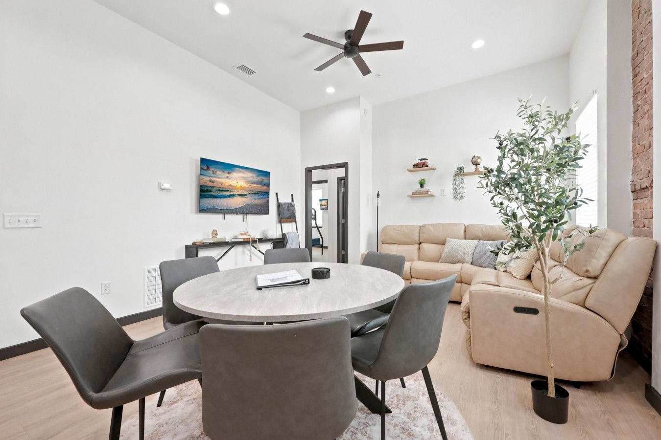 Un salon moderne avec une table ronde, des chaises grises, un canapé beige et un ventilateur de plafond.