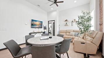 A modern living room with a round table, grey chairs, a beige sofa, and a ceiling fan.