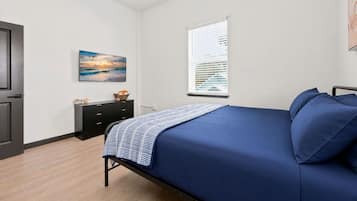 A bedroom with a bed, a dresser, a painting, and a window with blinds.