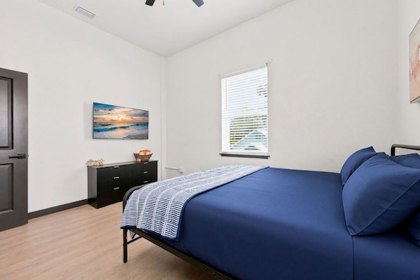 Un dormitorio con cama, cómoda, un cuadro y ventana con persianas.