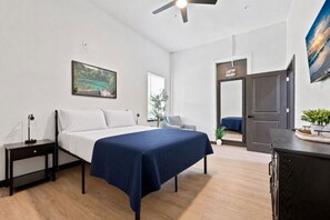 A bedroom with a bed, bedside table, and a nightstand. There is a window with a view of greenery and a door leading to another room. - High Springs Downtown | Steps to Dining & Shops (High Springs)