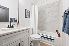 A modern bathroom with a white sink, a toilet, and a bathtub with a shower curtain. - High Springs Downtown | Steps to Dining & Shops (High Springs)
