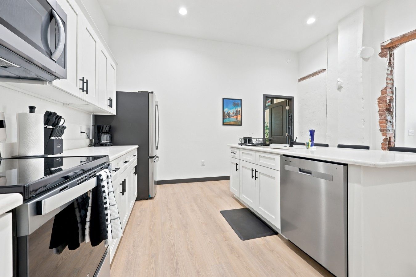 Una cocina moderna con electrodomésticos de acero inoxidable, armarios blancos y piso de madera.
