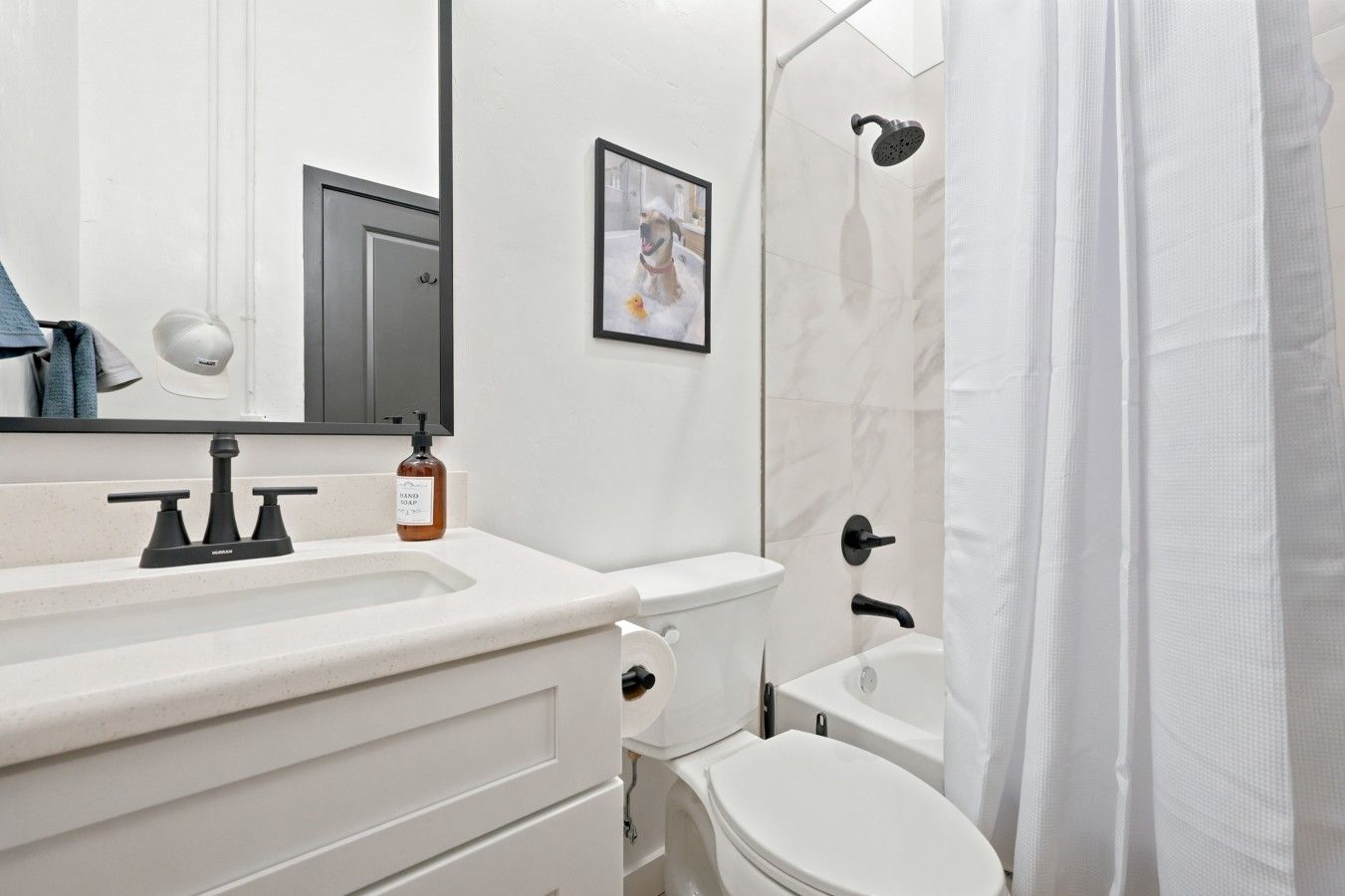 A modern bathroom with a white sink, a toilet, a shower with a rain showerhead, and a framed picture on the wall.