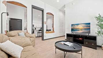 A modern living room with a sofa, a coffee table, a TV, and a kitchen in the background.