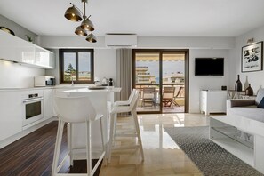 A modern kitchen with white appliances, a dining area with white chairs, and a living room with a sofa and a flat-screen TV. - Palm Beach Apartment Near Beach with Private Terraces, Parking, Wi-Fi, and Air Conditioning (Cannes)