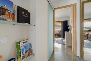 Un pasillo con una estantería, un atril para revistas y vistas a un salón con balcón.