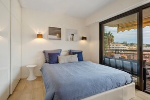 A bedroom with a bed, two wall-mounted lights, and a window overlooking a cityscape.
