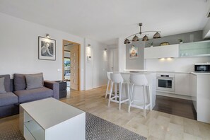 Una sala de estar moderna con un sofá, una mesa de centro y un comedor con sillas blancas, y una cocina al fondo.