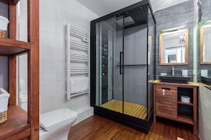 Et moderne badeværelse med en brusekabine i glas, et hvidt toilet og en trækommode med et spejl.